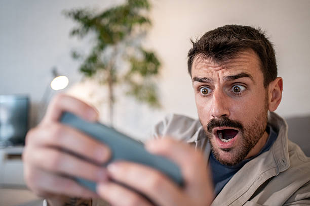 istock Shocked man playing mobile game at home 2209199400