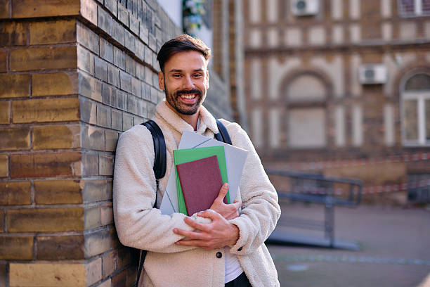 istock Smiling student holding books and leaning against a brick wall 2209213171