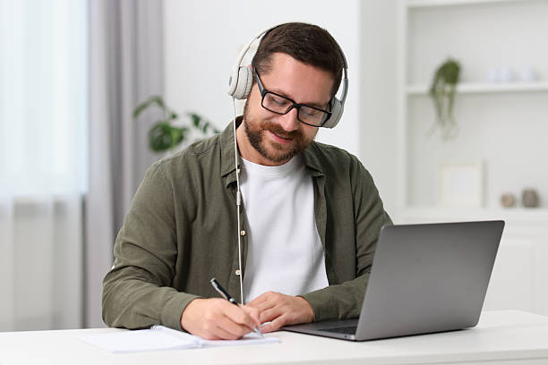 istock Interpreter in headphones taking notes while having video chat via laptop at white table indoors 2209215614