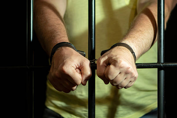 istock An arrestee with clenched fists and handcuffed behind bars. 2209230768