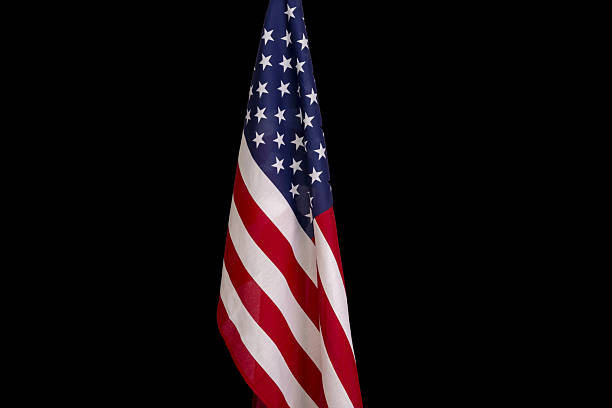 istock The American flag is mounted on a flagpole, black background, medium plan. 2209230873