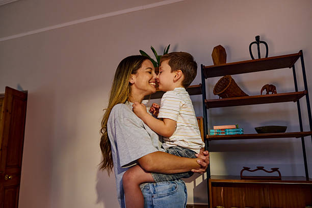 Mother holding her son in her arms and rubbing noses, inside their home, showing love and affection