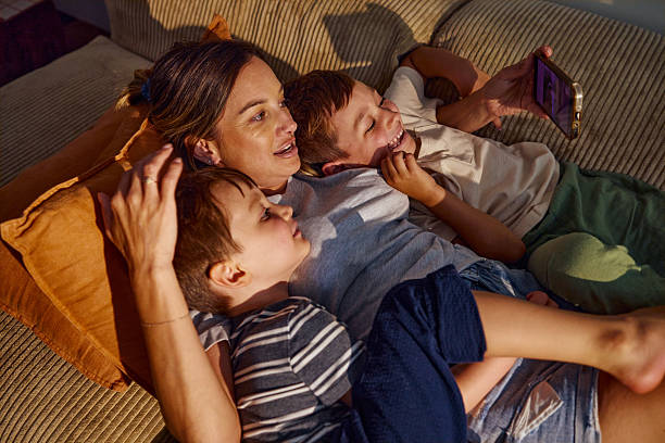istock Happy mother embracing two sons while watching smartphone on sofa 2209231462