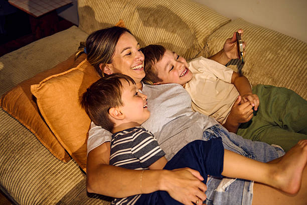 istock Happy mother embracing two sons while watching smartphone on sofa 2209231463