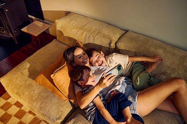Happy mother embracing two sons while watching smartphone on sofa