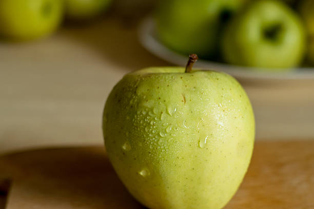A close-up of a beautiful green apple. Juicy green apples are in the background. Still life of apples.