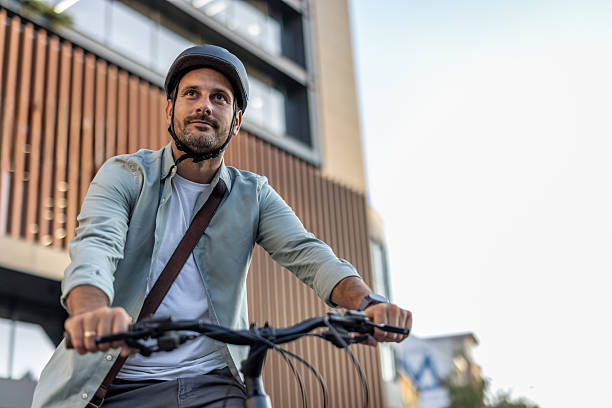 istock Businessman riding bicycle in urban setting while wearing helmet 2209249824