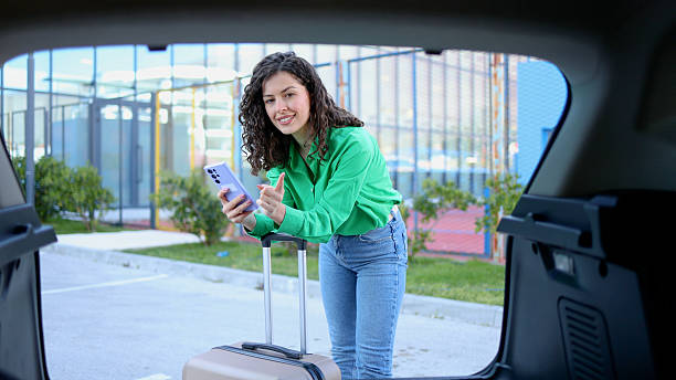 istock Woman loading luggage in car trunk, checking smartphone screen during travel preparation 2209254203