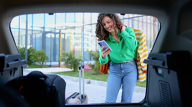 istock Young woman loading luggage into car trunk while using her phone 2209254205