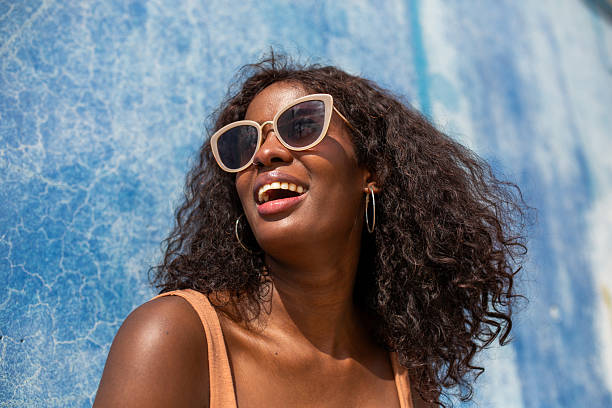 istock Smiling black woman with sunglasses by blue wall 2209259654
