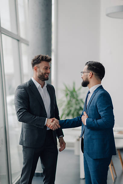 istock Two smiling businessmen shaking hands in modern office 2209259912