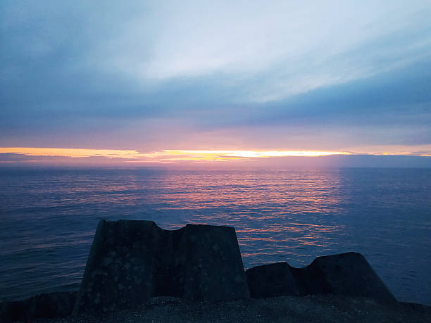 istock Serene seascape at dusk. Calm, reflective water under a colorful sky. Concrete structure adds depth. Ideal for travel, nature, or contemplation themes. 2209260370