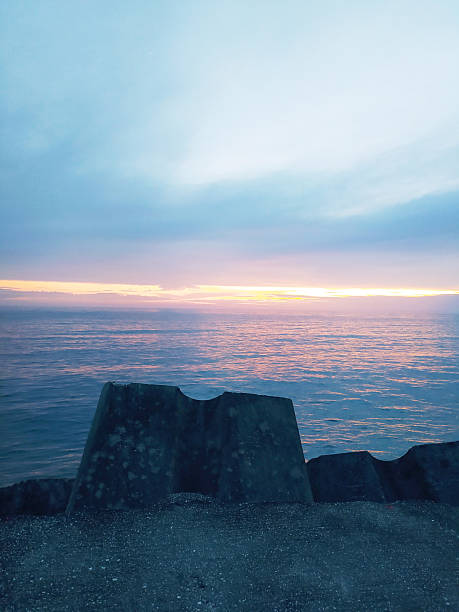 Serene seascape featuring coastal defenses at dawn. Ethereal light reflects on calm waters. Evokes tranquility and resilience. Ideal for travel or nature themes.