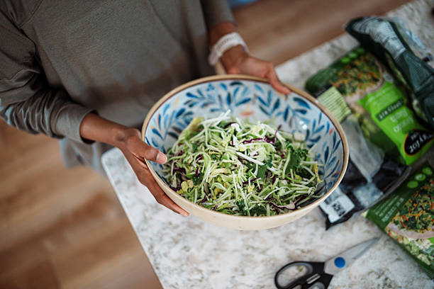 High angle view looking down at a beautiful ceramic serving bowl filled with salad in the hands of an unrecognizable woman of Indian descent who is hosting in her home family visiitng for the weekend.