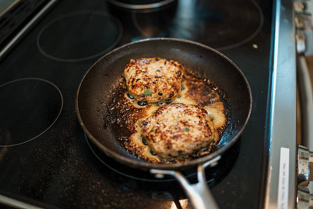 High angle view looking down at two pieces of meat cooking in a frying pan on an electric stovetop in a domestic kitchen.