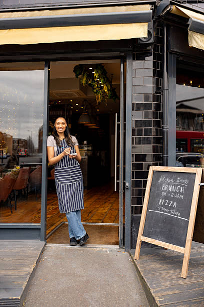 istock Waitress standing on the door at a sidewalk cafe holding a notepad 2209273710
