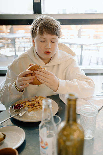 istock Teen boy mid-chew with burger at cafe 2209273823