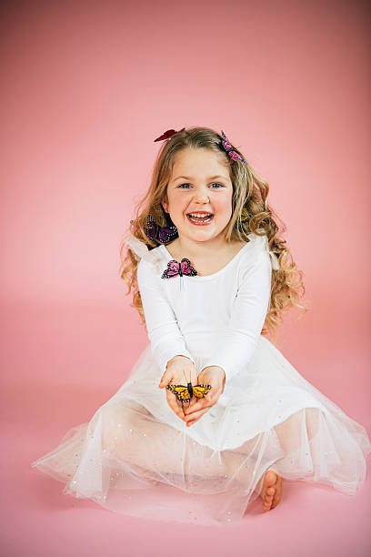 Laughing girl holding butterfly while sitting on pink floor in North Andover, Massachusetts, United States