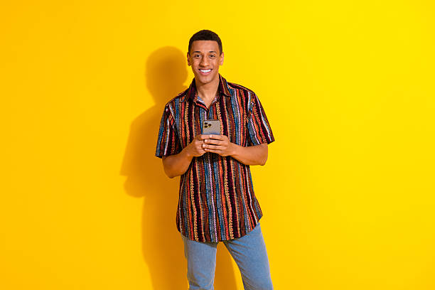 istock Smiling young man using smartphone against vibrant yellow background showcasing trendy casual fashion and cheerful lifestyle 2209306915