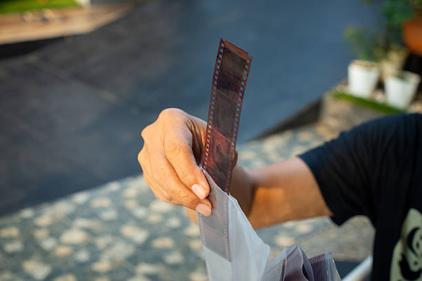 Southeast Asian middle-aged man holding undeveloped negative film strips, checking in outdoor environment through sun light in the morning