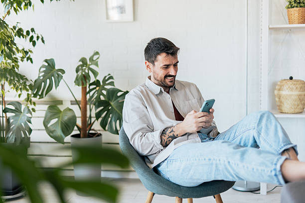 istock Young man relaxing at home, using his smartphone and smiling 2209307932