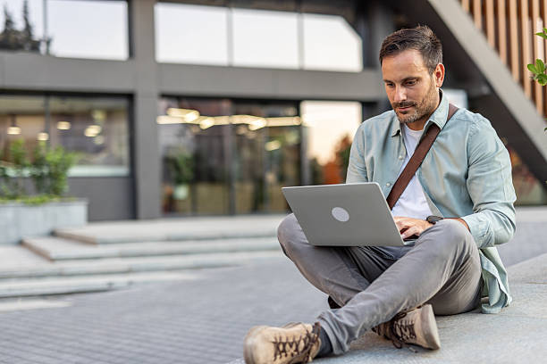 istock Businessman working remotely with laptop outside modern office building 2209307949