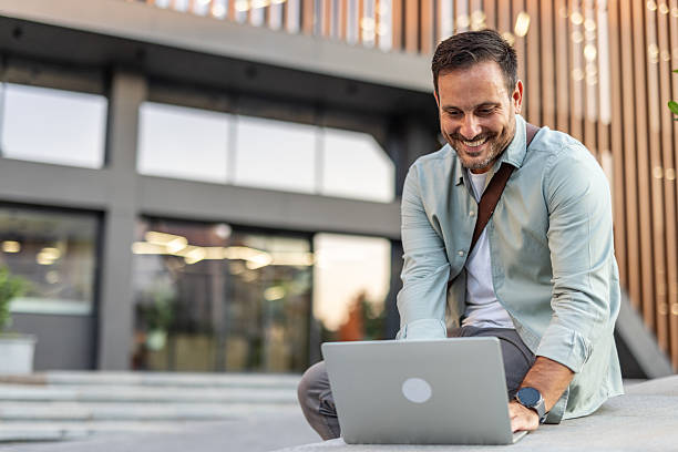 istock Smiling businessman working on laptop outside modern office building 2209307953