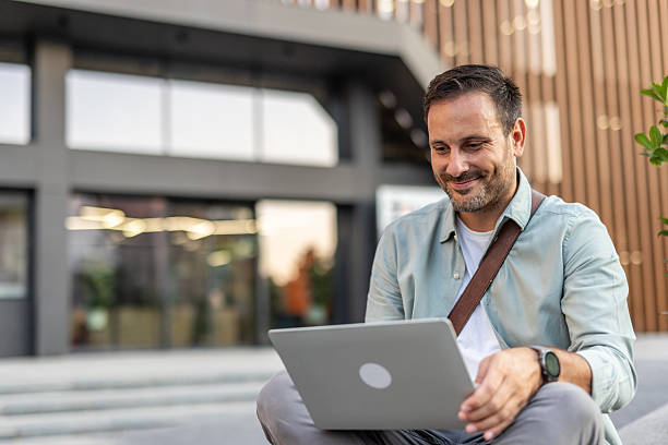 istock Smiling businessman working on laptop outside modern office building 2209307969
