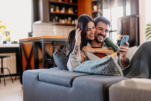 istock Happy couple relaxing on sofa and using smartphone at home 2209307996
