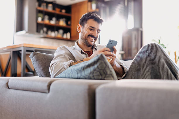 istock Young man is relaxing on the sofa, using smartphone and smiling 2209307997