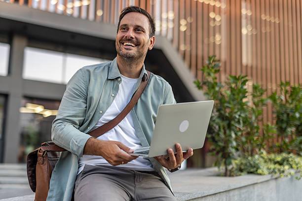 istock Smiling businessman working remotely with laptop outside office 2209308011