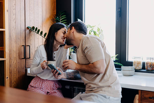 istock Young couple kissing in the kitchen while having breakfast and checking the phone 2209308132