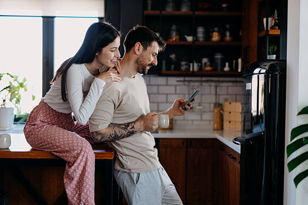 istock Young couple using phone and drinking coffee in the kitchen 2209308882