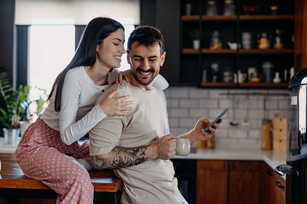 istock Young couple using phone and smiling in kitchen 2209308888