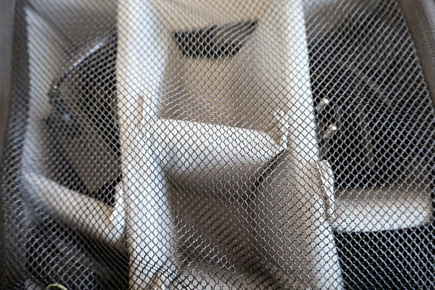 Abstract close-up of black mesh fabric with a blurred light object in the background. The texture of the mesh is clearly defined, forming a diamond-shaped pattern.