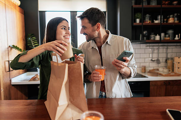 istock Young couple unpacking takeaway food in kitchen and using phone 2209310022