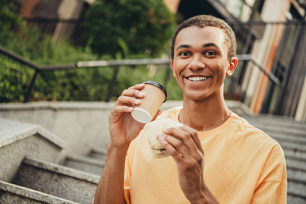 istock Young man enjoying a coffee and sandwich outdoors on city steps during a sunny day 2209310285
