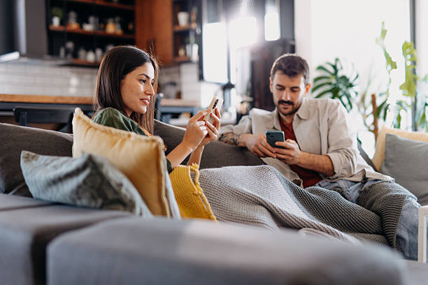 istock Young couple relaxing on sofa, browsing internet on smartphones 2209311771