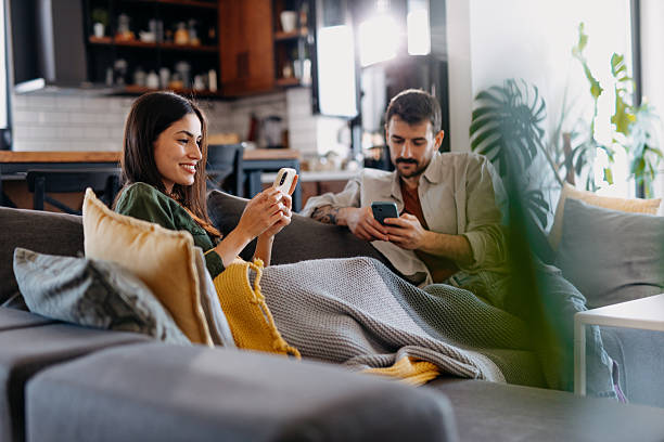 istock Young couple relaxing on the sofa, browsing on their smartphones 2209311790