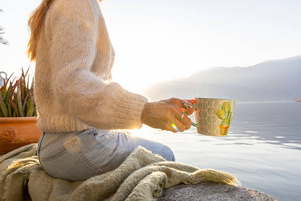 Woman Relaxing by Lakeside Holding Coffee Cup