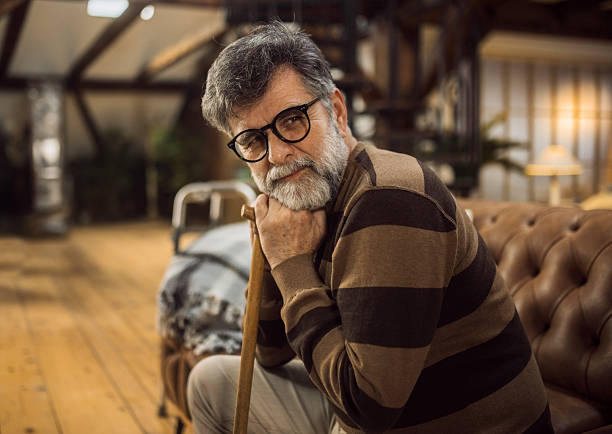 Thoughtful elderly man sitting alone at home with his walking cane