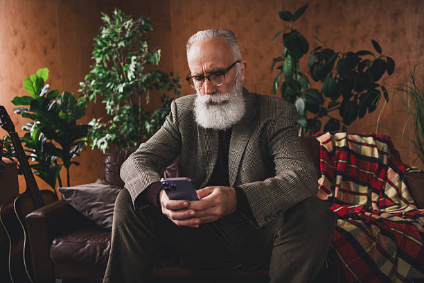 istock Stylish elderly man in a vintage interior using smartphone, surrounded by houseplants and retro decor 2209316119