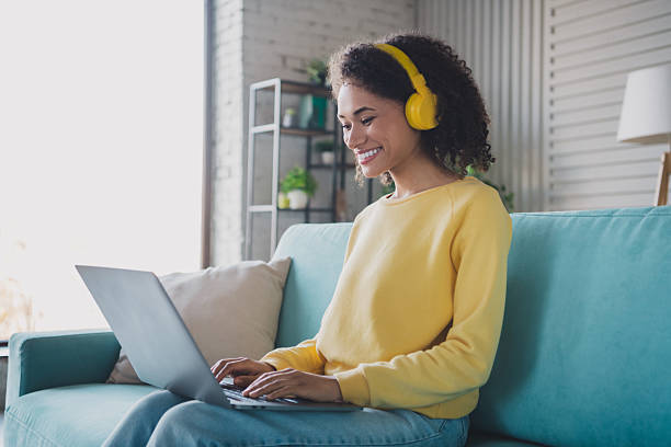 istock Young woman with headphones enjoying leisure time on a sofa while using a laptop at home 2209316197