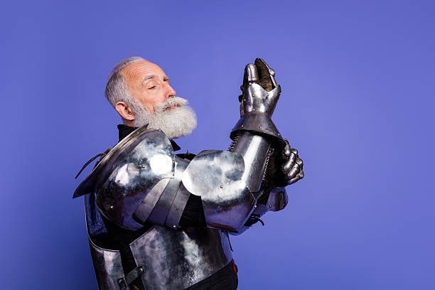 istock Elderly man in medieval knight's armor posing against violet background 2209317017