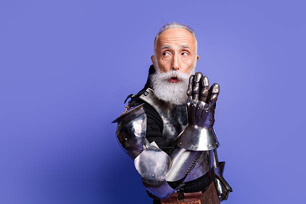 istock Elderly man in medieval knight's armor posing against violet background 2209317019