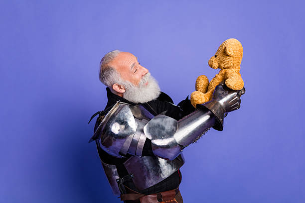 istock Bearded knight in shining armor holding a teddy bear against a purple backdrop, blending medieval themes with modern playful humor. 2209317026