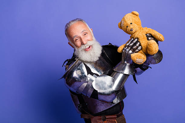 istock Mature bearded warrior in knight armor holds a teddy bear against purple backdrop 2209317035