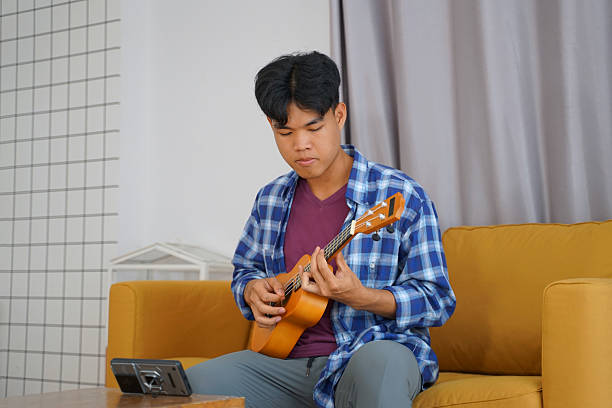 istock Young man is playing ukulele in living room. 2209323059