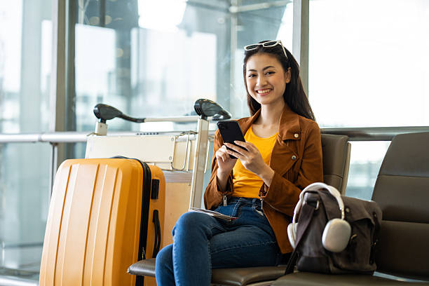 istock Young asian woman traveler using smartphone for checking flight information and playing social media app for shopping online while waiting with her luggage at the airport terminal. 2209323766