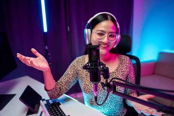 istock Content creator woman host streaming her a podcast with headphones and microphone interview cheering guest conversation broadcast studio with neon light. Blogger motivation recording voice over radio 2209324348